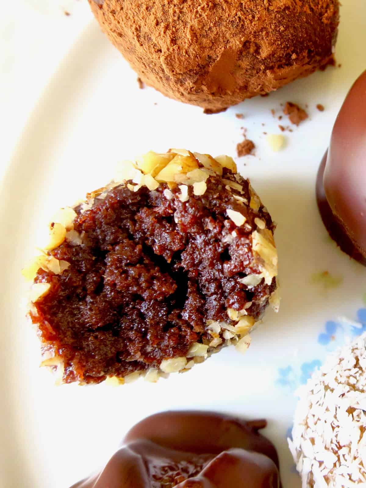 Chocolate cake ball cut in half with focus on the inside of the chocolate cake ball. A few other cake balls with different coatings in view also.