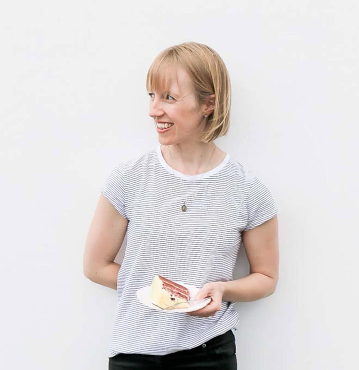 Sarah holding a piece of cake on a plate.