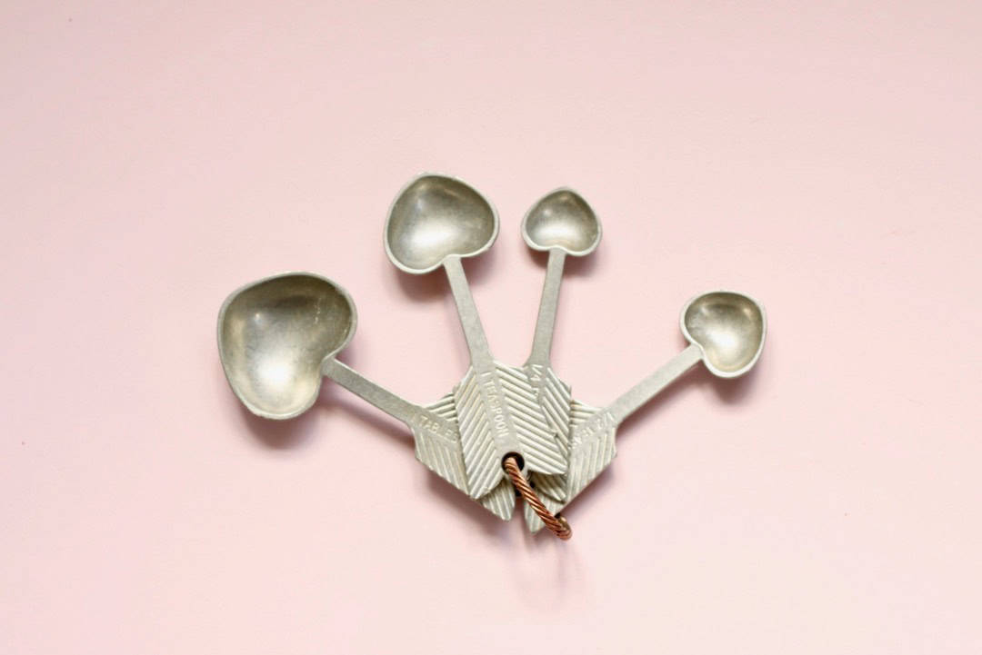 Love-heart shaped measuring spoons, spread out with pink background