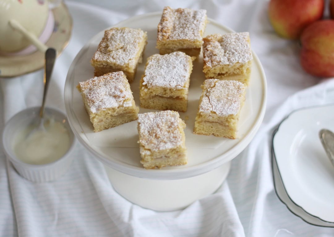 Pieces of apple shortcake on a cake stand with plates and yoghurt on the side