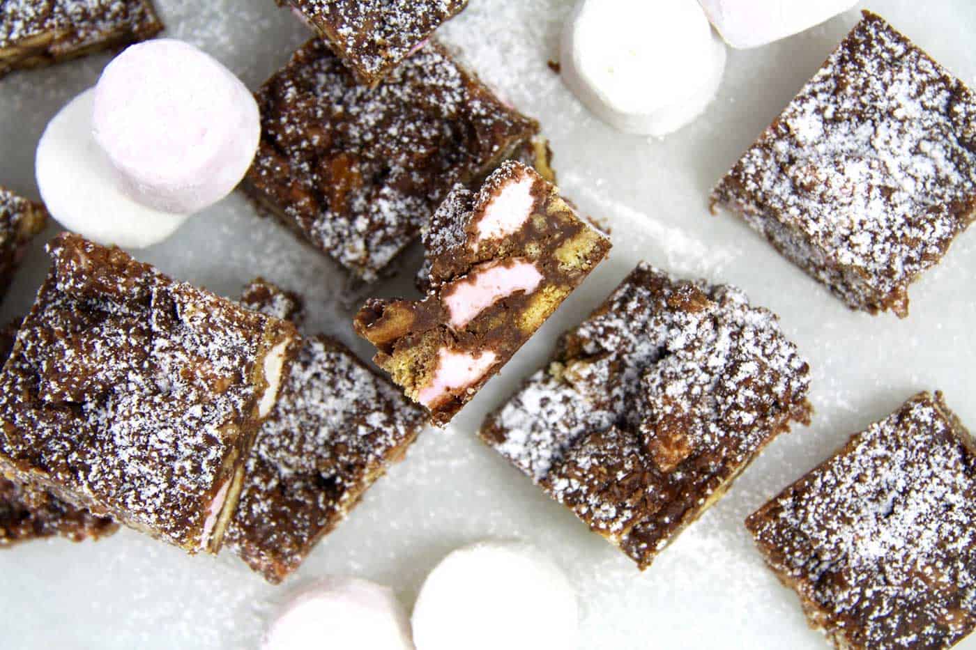 Pieces of rocky road with one on the side and marshmallows around it.