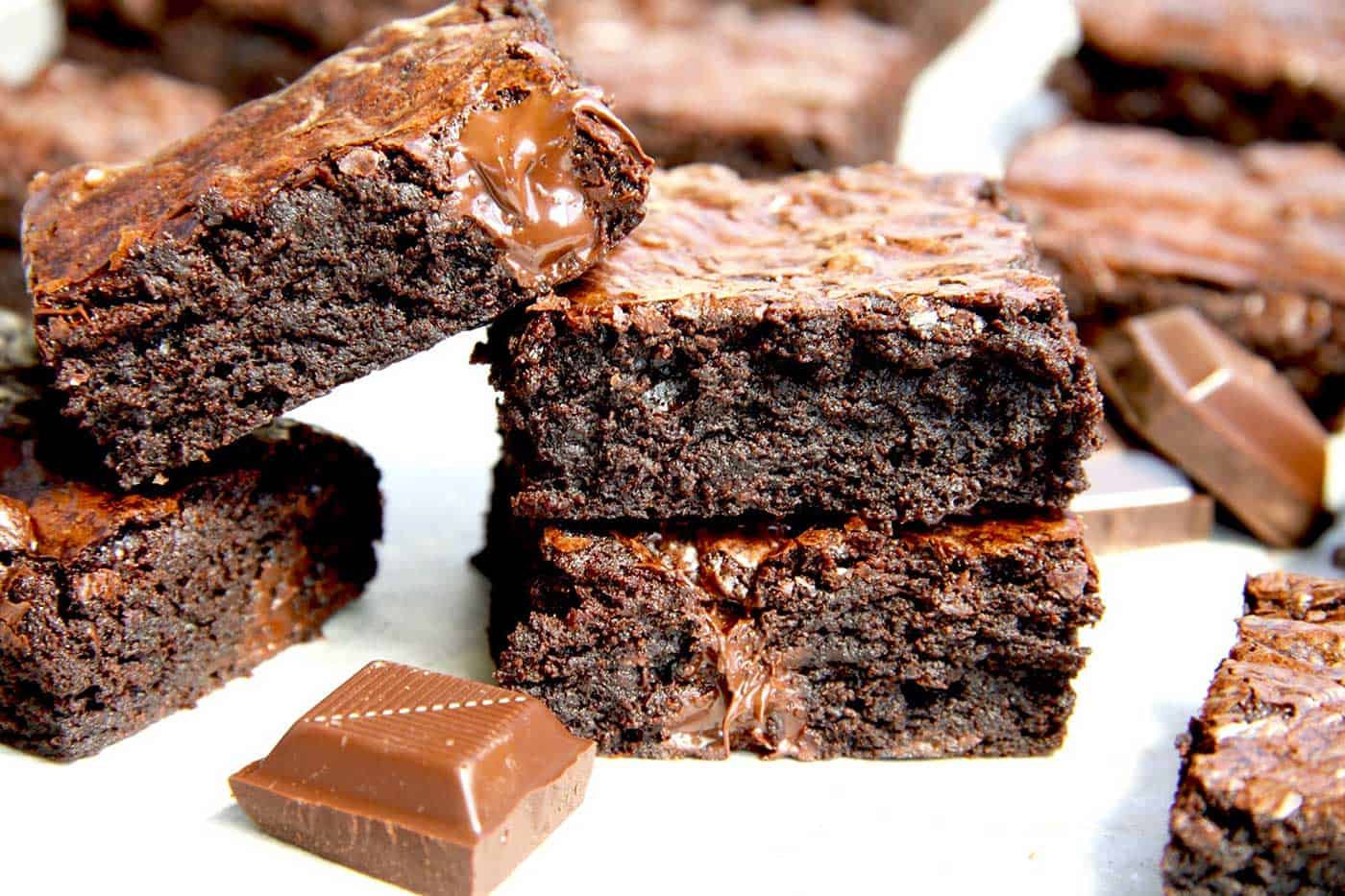 Fudgy cocoa brownie's leaning against each other with pieces of chocolate next to them