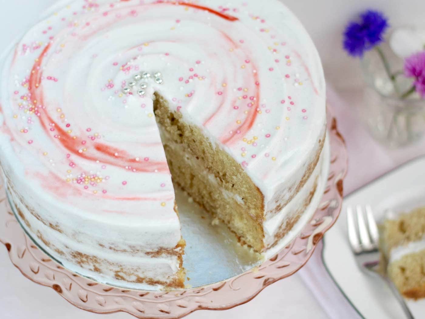 Fully iced dairy gluten vanilla cake on cake stand with a slice taken out of it