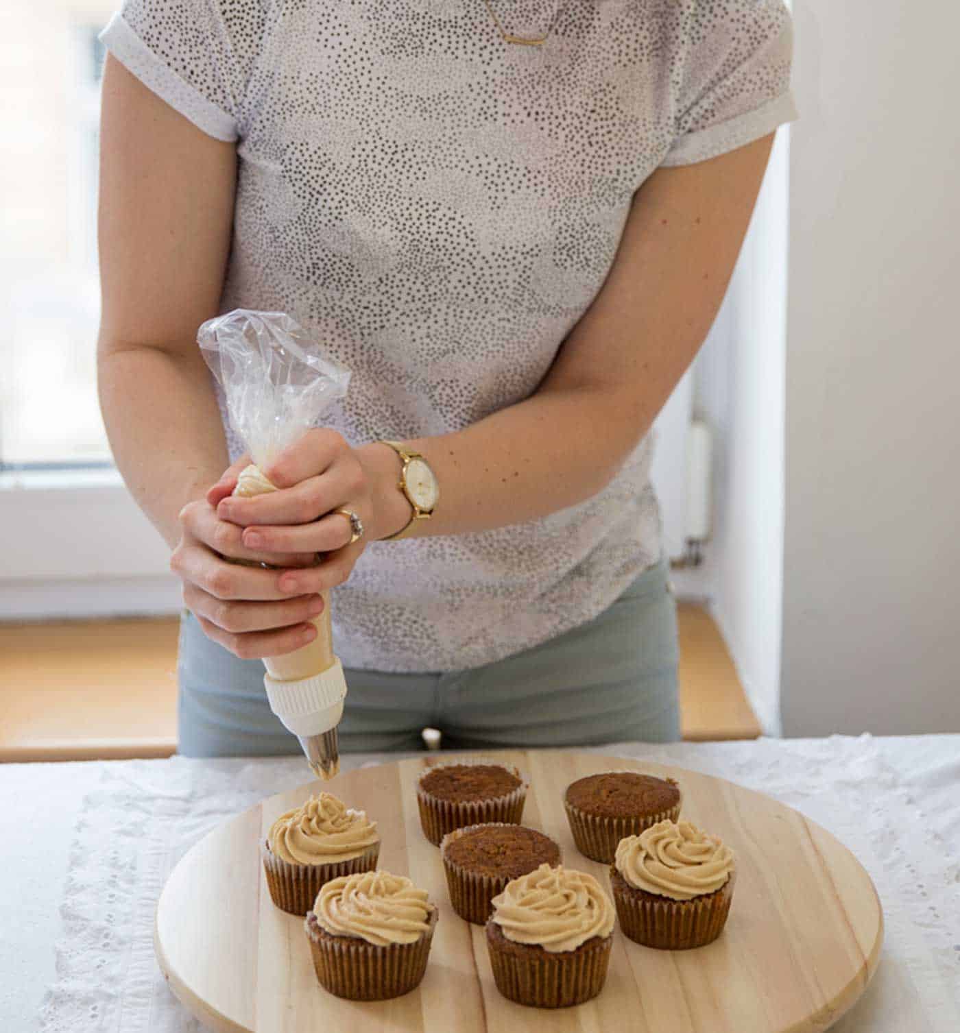 A person piping icing onto the cupcakes.