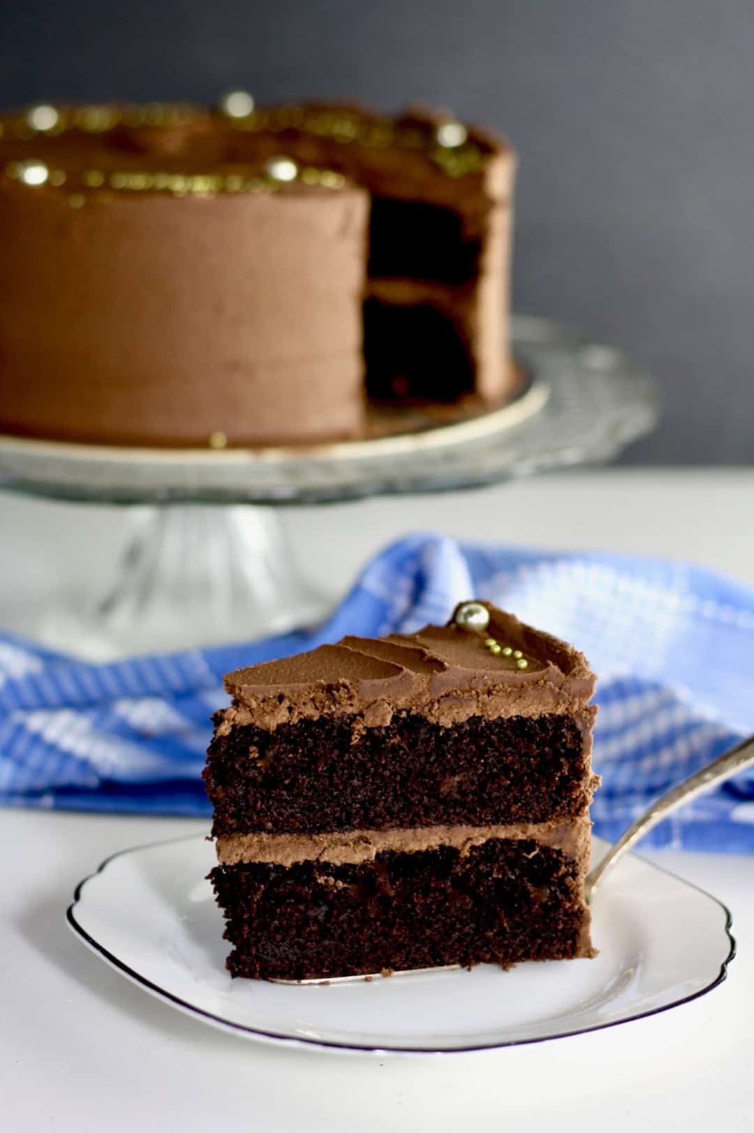 A slice of chocolate cake with the rest of the cake in the background.