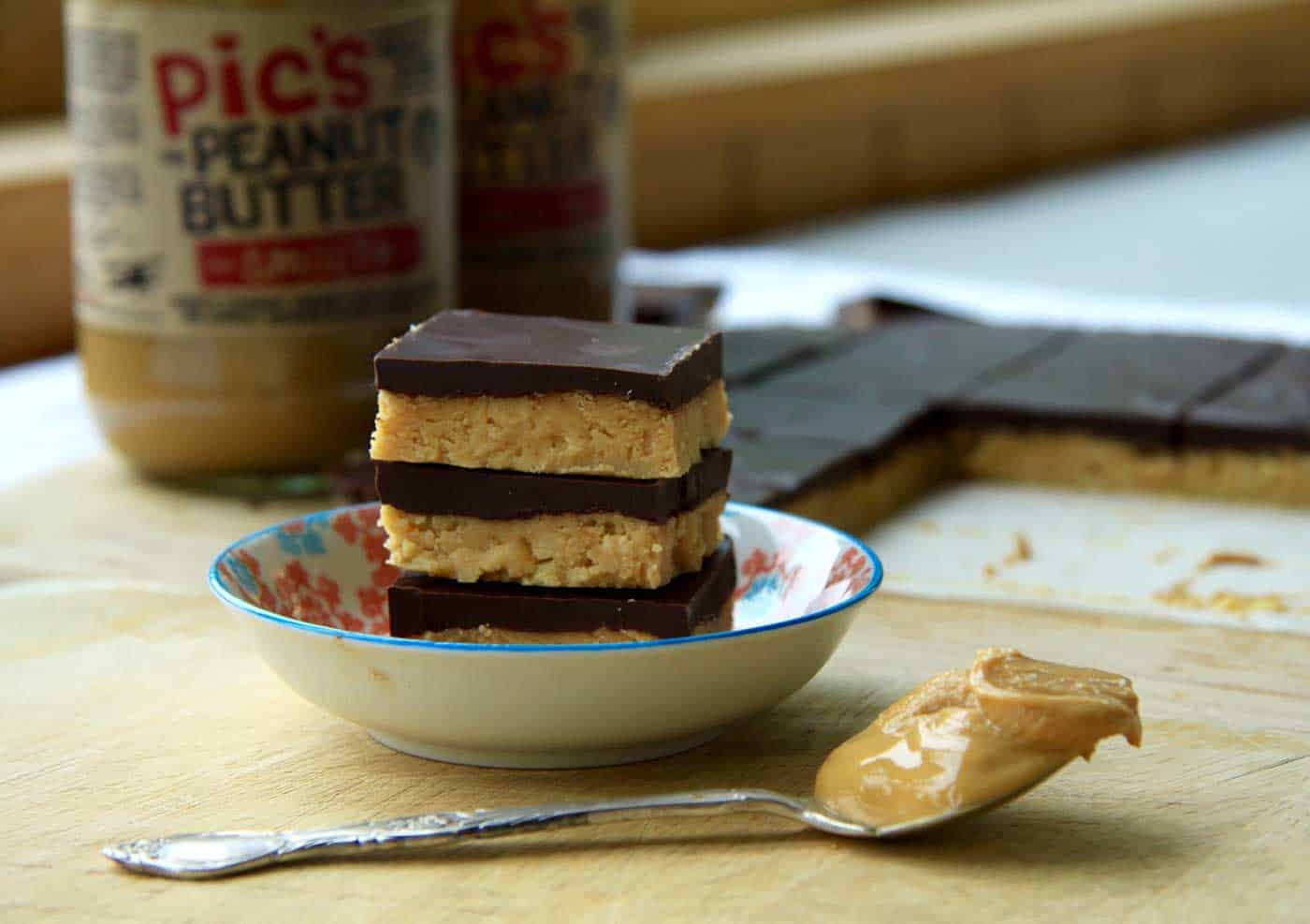 A little bowl with a stack of bars in it and teaspoon of peanut butter next to it