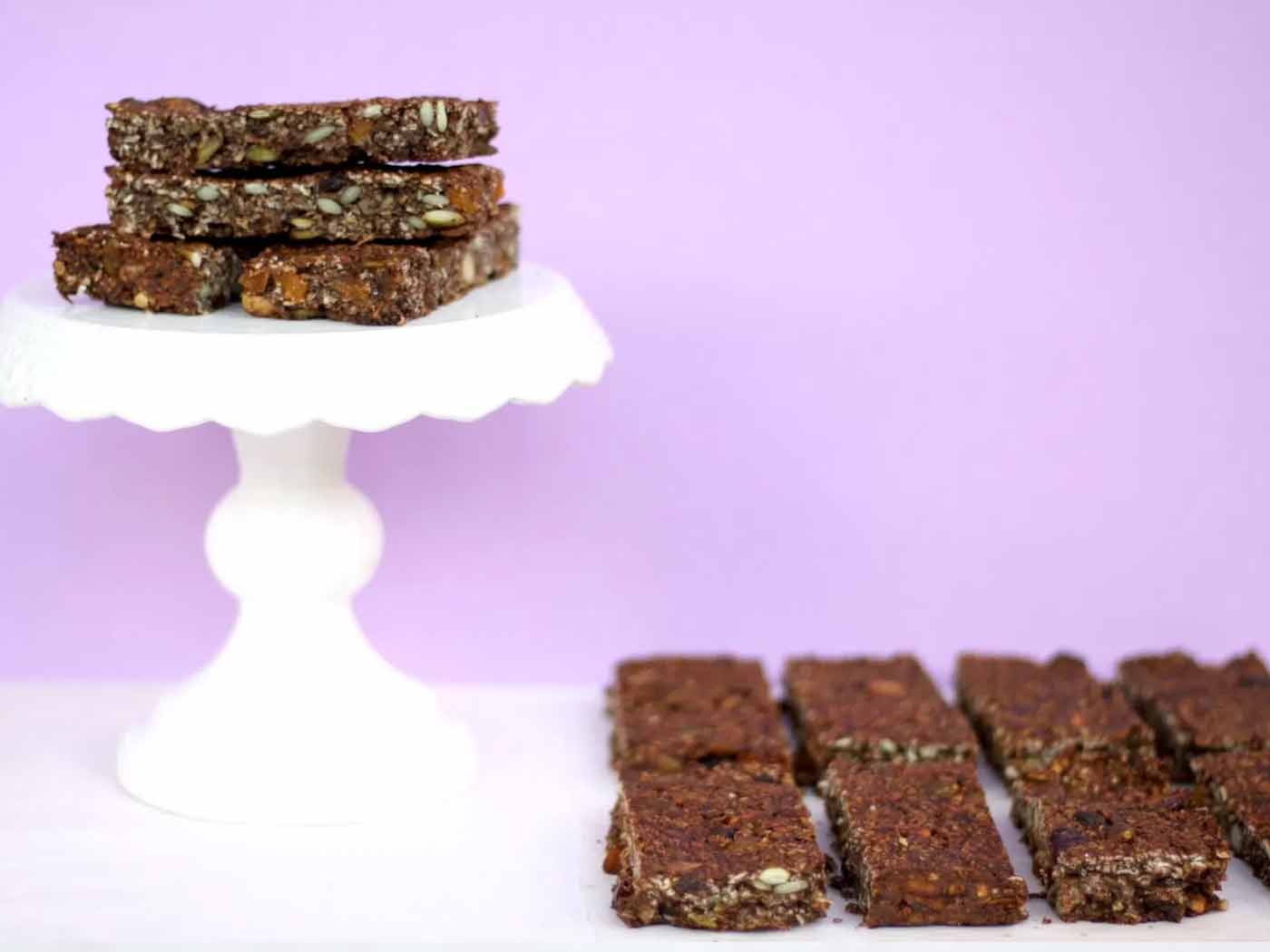 A white cake stand with granola bars sitting on it and also some next to it.