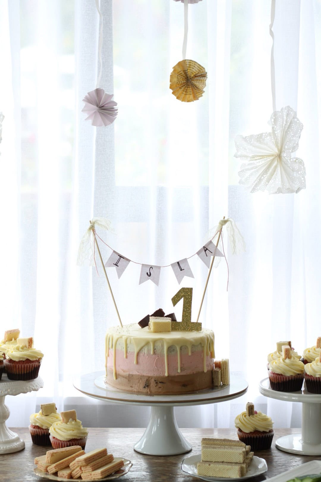 A table with Neapolitan cake and cupcakes on it.