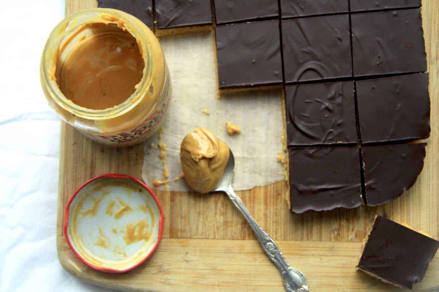Peanut butter jar opened with a teaspoon of peanut butter and slice next to it