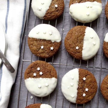 Ginger cookies on a cooling rack. Each cookie has white icing on half of the cookie with white srpinkles.
