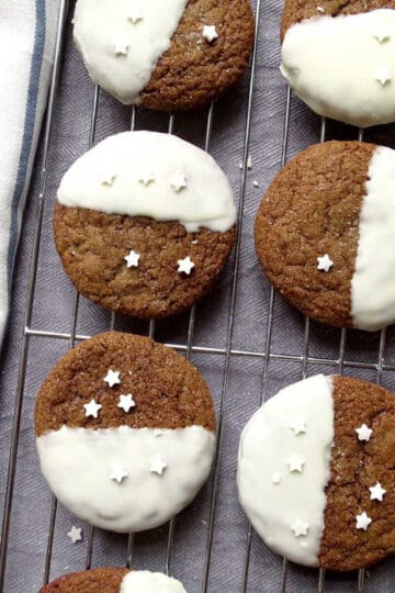 Ginger cookies on a cooling rack. Each cookie has white icing on half of the cookie with white srpinkles.