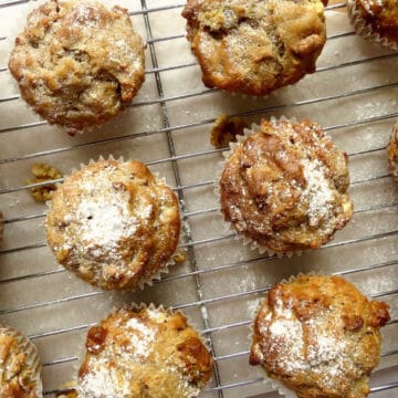 Apple walnut muffins on a cooling rack. They are sprinkled with icing sugar.
