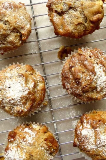 Apple walnut muffins on a cooling rack. They are sprinkled with icing sugar.