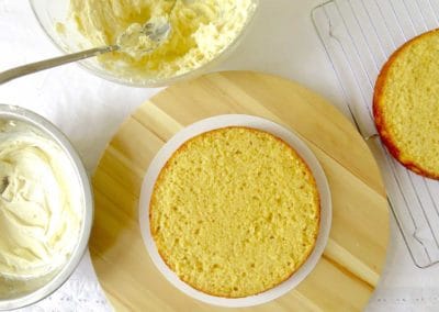 Levelled vanilla cake layers with a bowl of buttercream ready to be applied to the cake layers.