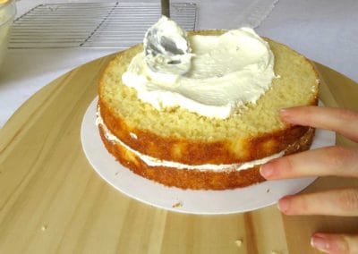 White buttercream frosting being applied to the layers of vanilla cake.