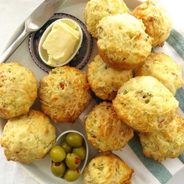 Fluffy cheese and ham muffins on a striped green t-towel. Olives and butter on the side.