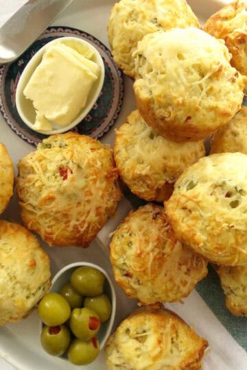 Fluffy cheese and ham muffins on a striped green t-towel. Olives and butter on the side.