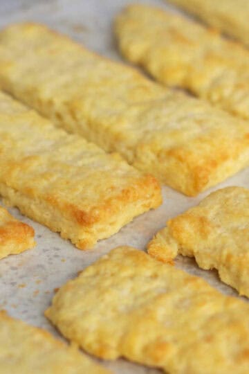 Flaky baked cheese straws lined up on a baking tray.