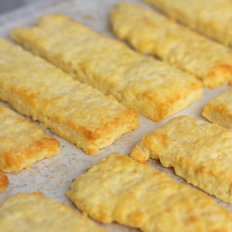 Flaky baked cheese straws lined up on a baking tray.