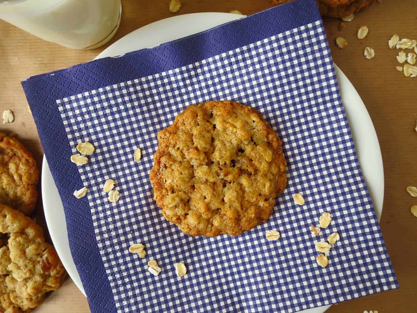 Oatmeal cookie on a plate with a blue checkered napkin and extra oats sprinkled around.