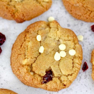 A moorish white chocolate cranberry cookie sitting on a baking sheet with more in the background.