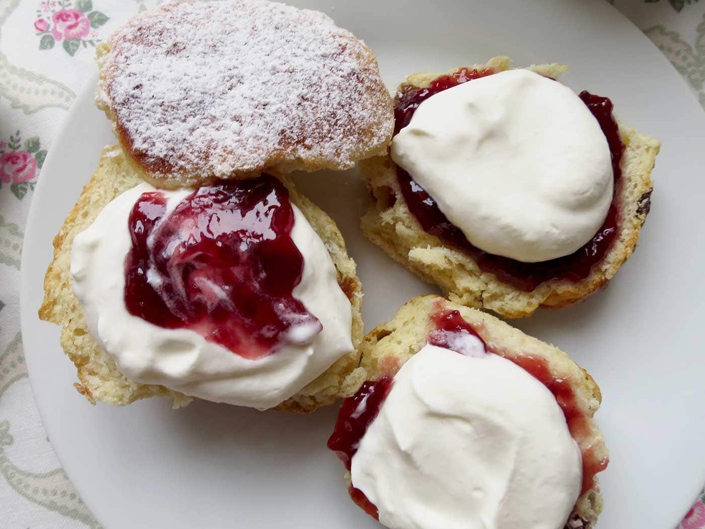 A close up of two scones, cut in half and lathered with whipped clotted cream and jam. Devonshire and Cornish-style.