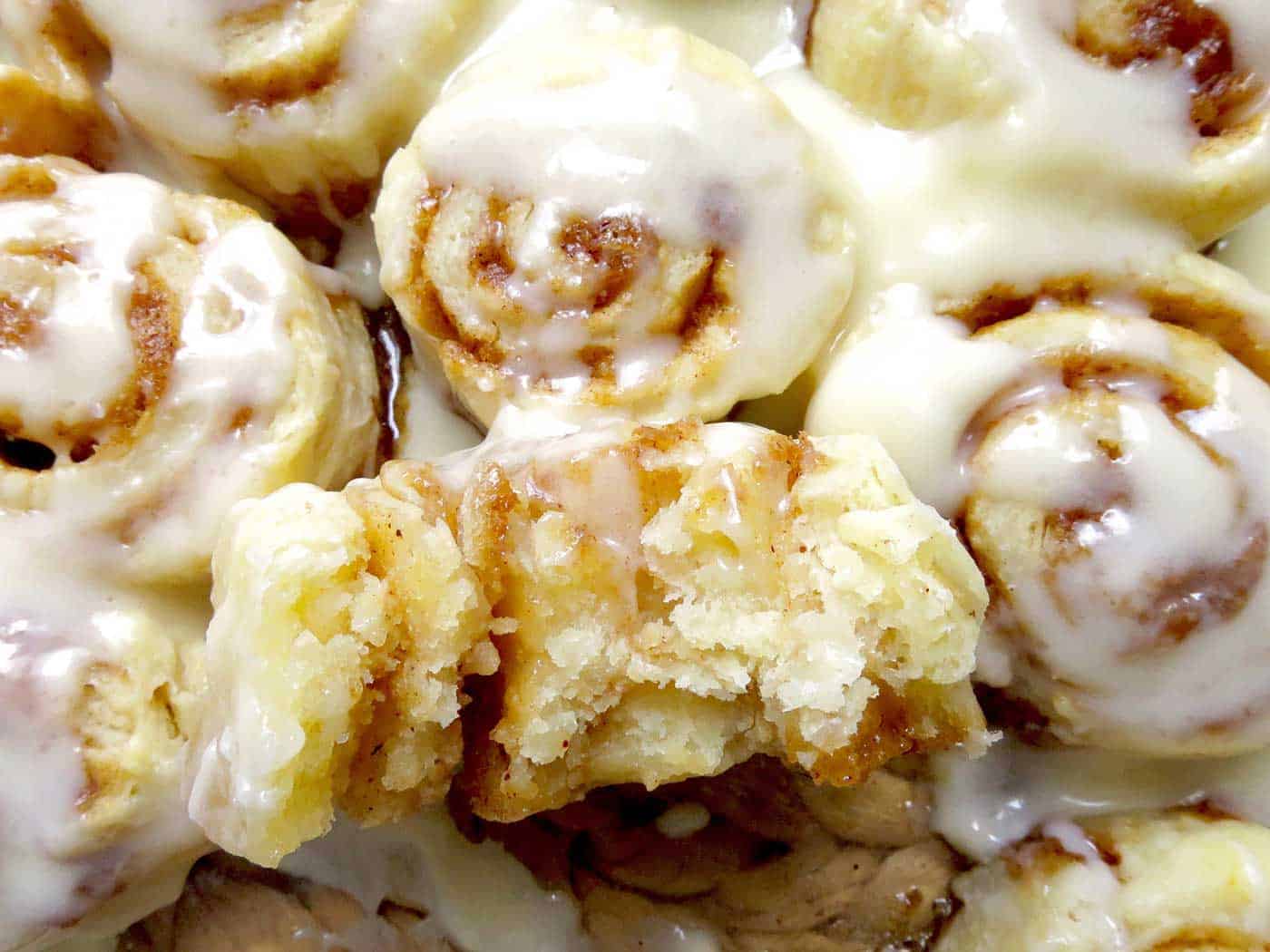 A tray of cinnamon rolls with one sitting on top that has been broken in half.