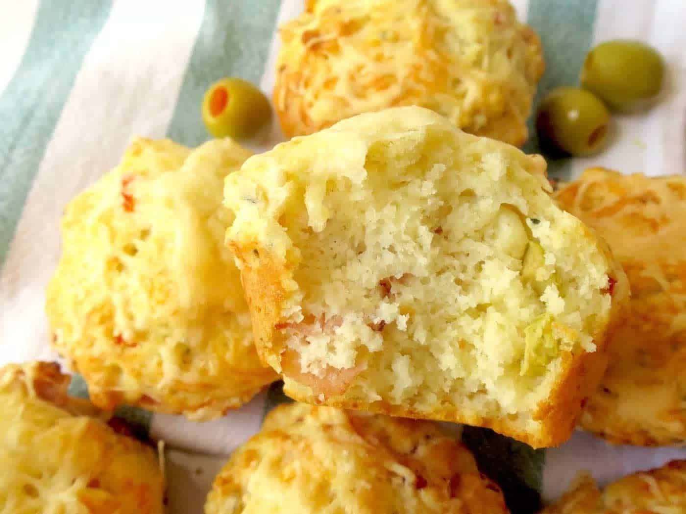 A cheese and olive muffin cut in half sitting on a tea towel of other muffins.