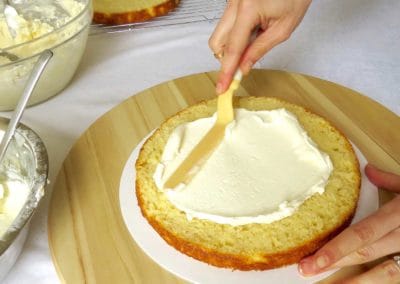One layer of vanilla cake with a person using a a spatula to spread a layer of buttercream frosting on it.