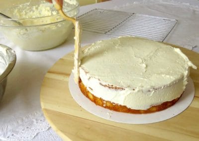 Vanilla buttercream frosting being applied to the vanilla cake layers.
