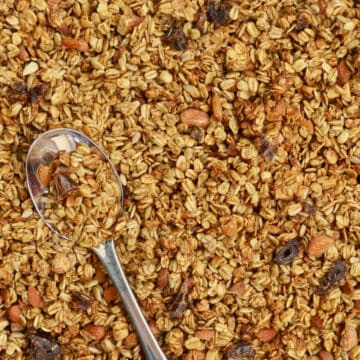 A spoon nearly lost inside a big batch of crunchy Gingerbread Granola. It is loaded with almonds, oats and dates.