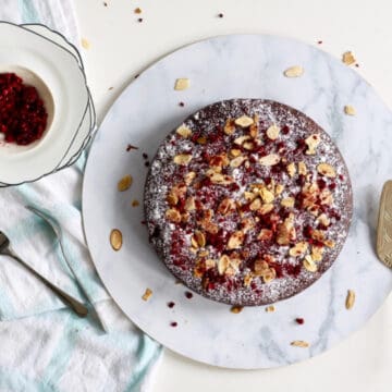 Top view of gluten dairy free almond raspberry cake. It is decorated with sliced almonds and freeze dried raspberries.