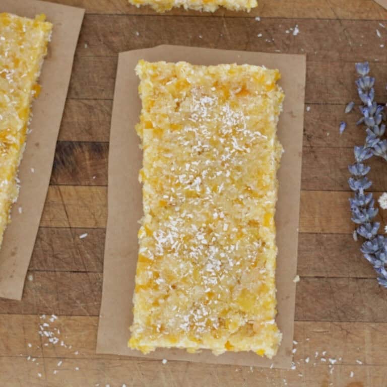 A piece of apricot almond slice on a board and a piece of lavender sitting next to it.