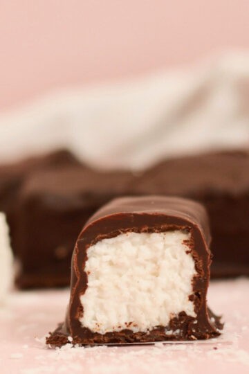 A perfectly formed homemade bounty bar which has been cut in half. It showcases an outer casing of chocolate which is filled with coconut bounty filling.