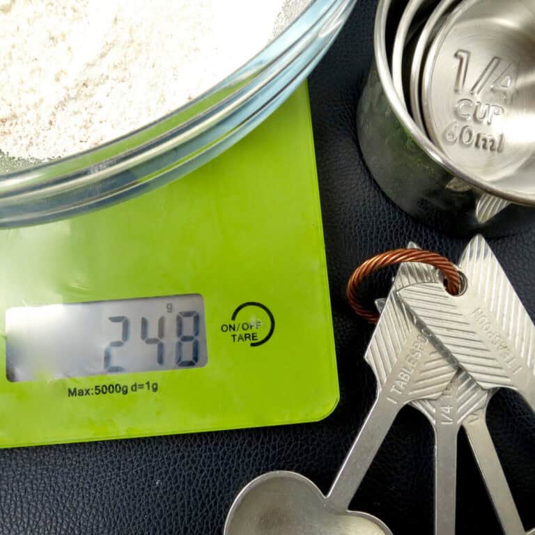 Green digital scales with a bowl of flour on top. Next to it are measuring cups and measuring spoons.