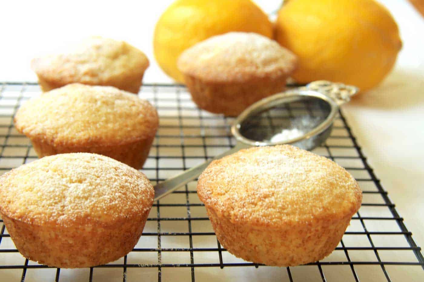 Lemon cream cheese muffins on a cooling rack with lemons in background.