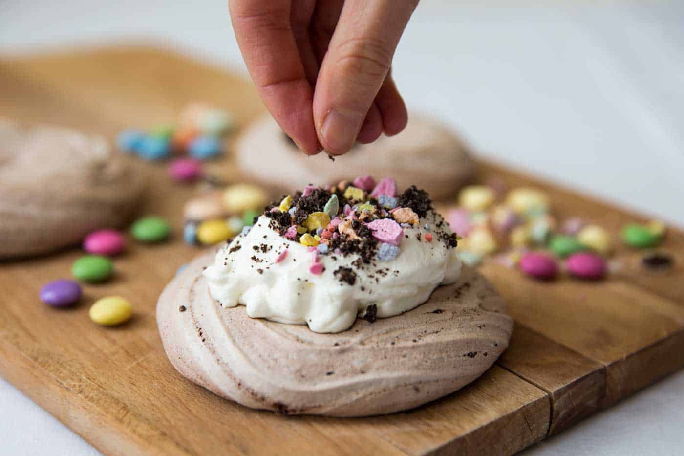 A hand sprinkling sweets on Easter meringue nests.