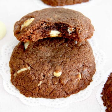 Fudgy Nutella cookies with a bite taken out of one. They are filled with white chocolate chunks.