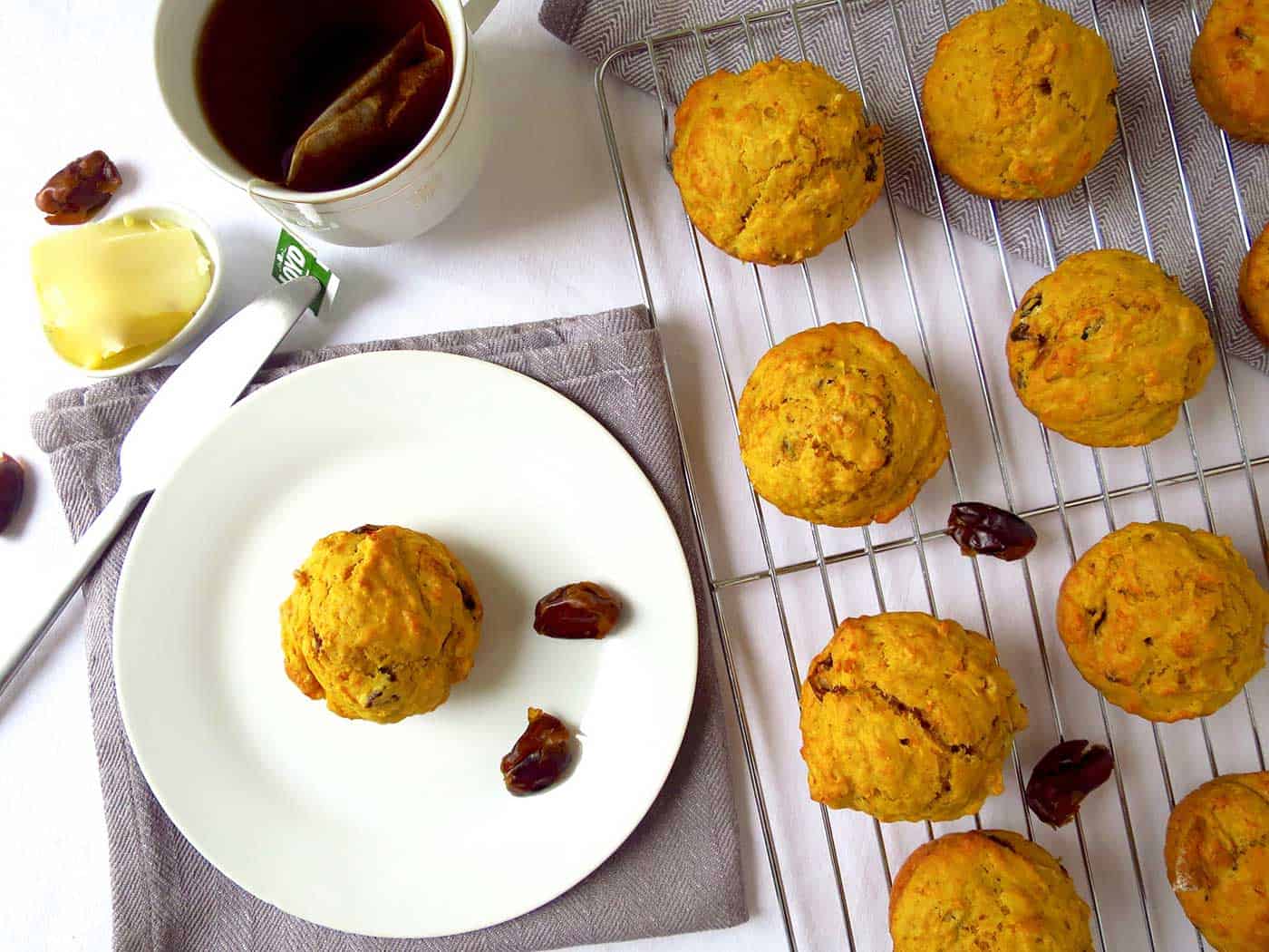 A cup of tea, plate with muffin and cooling rack of remaining muffins.