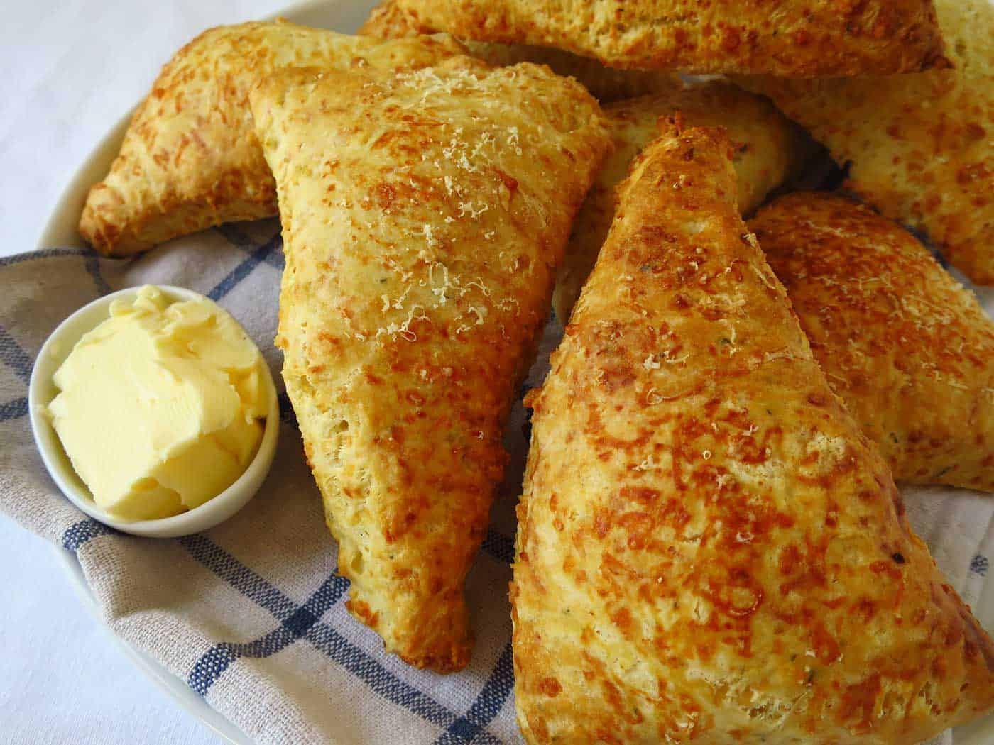 Triangle shaped cheese scones ready to be cut in half and a dish of butter on the side.