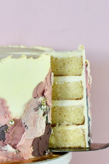 A beautifully iced four layer gluten free cake. A piece is about to be served.