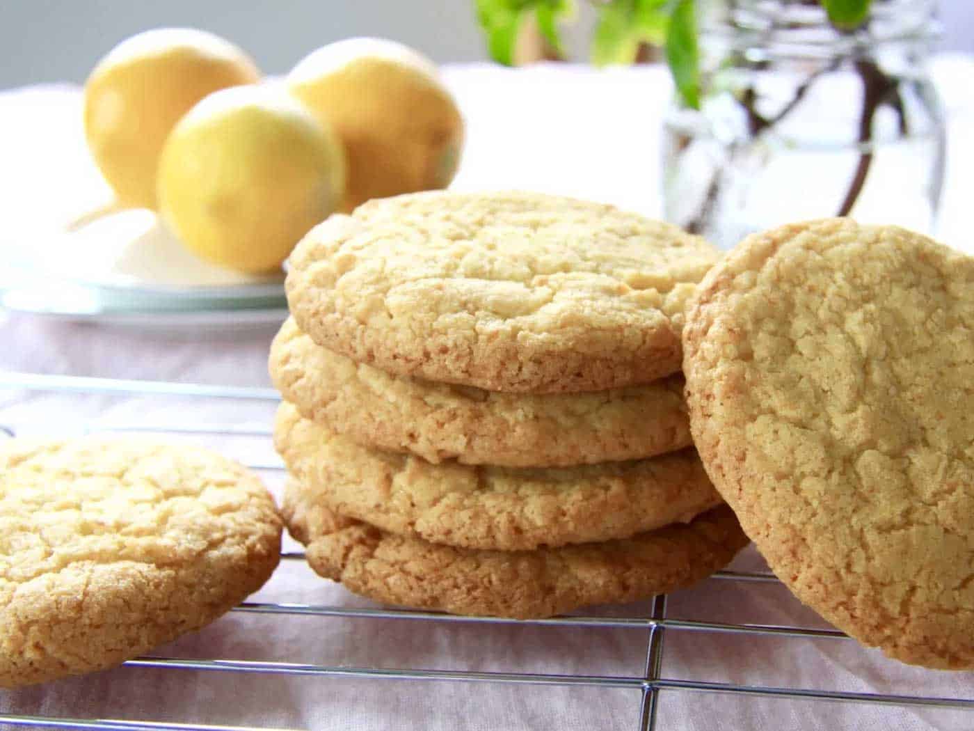 A stack of cookies cooling on a cooling rack. Lemons and flowers in background.