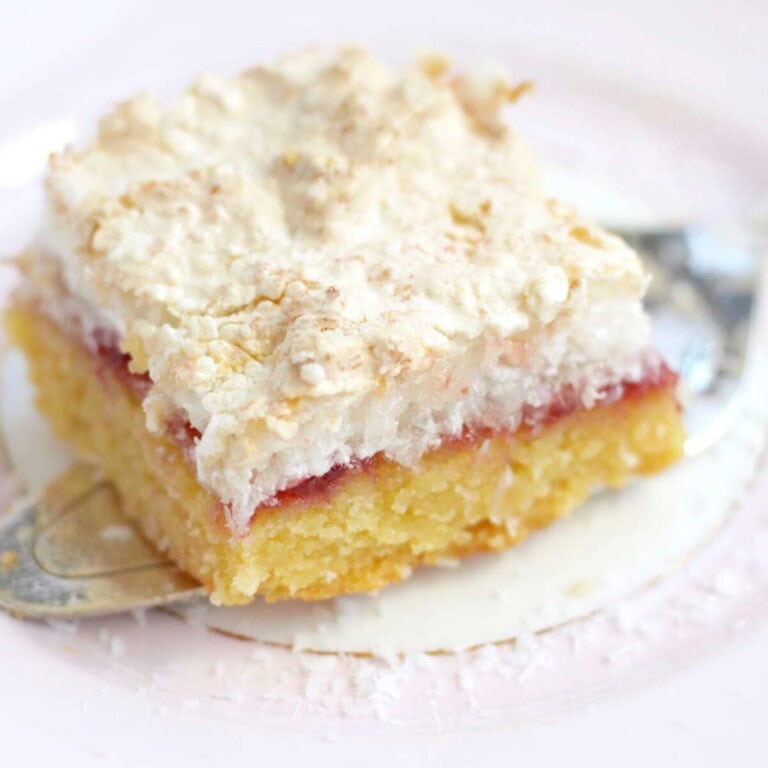 A beautiful piece of Louise Cake Slice sitting on a cake server. It has a vanilla base, berry filling and a fluffy meringue topping.