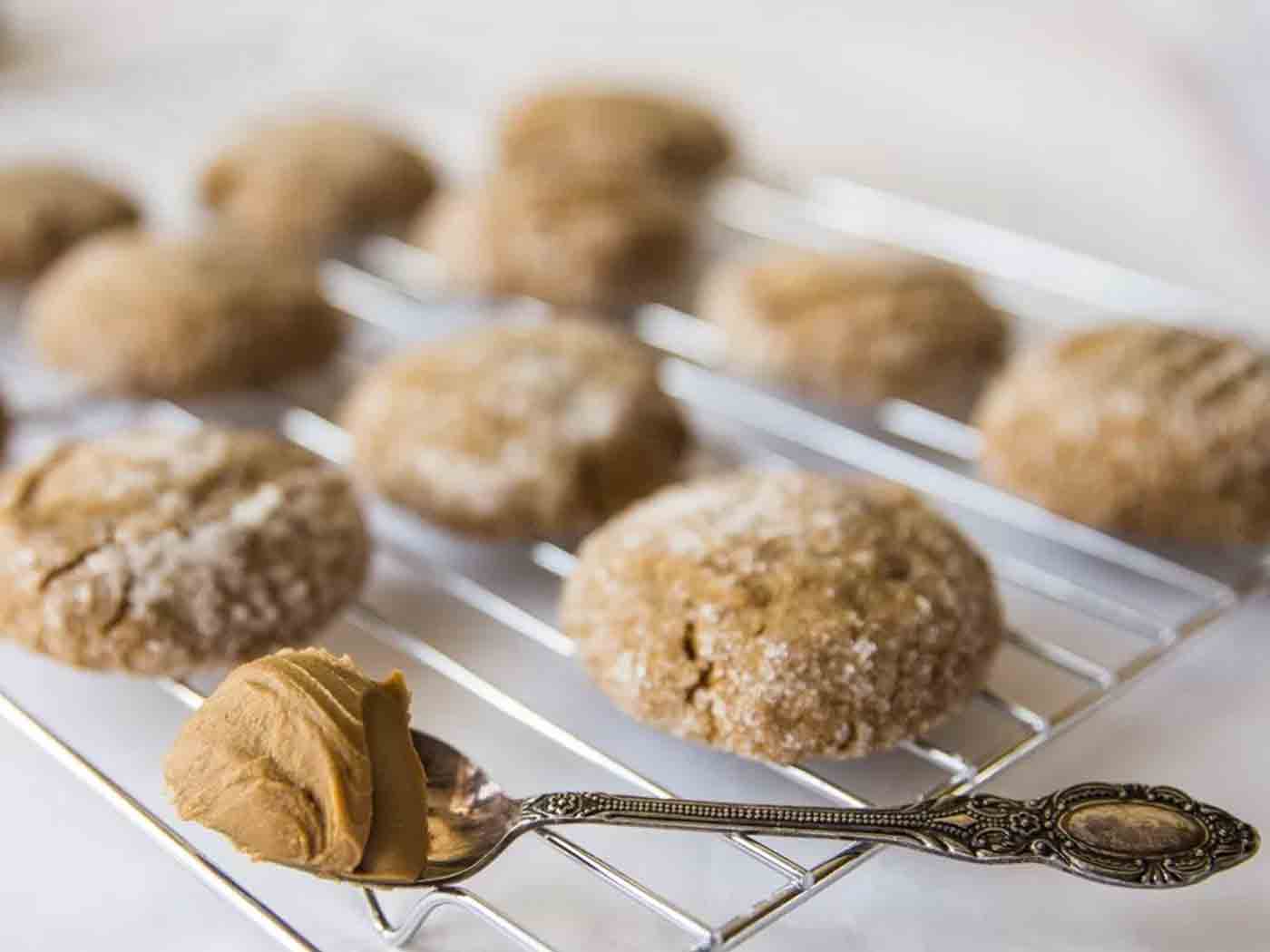 A teaspoon of Biscoff with cookies cooling on a cooling rack in the background.