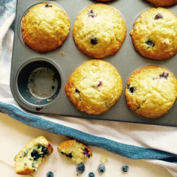 Cafe style blueberry lemon muffins in muffin tin with one taken out.