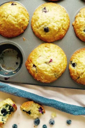 Cafe style blueberry lemon muffins in muffin tin with one taken out.