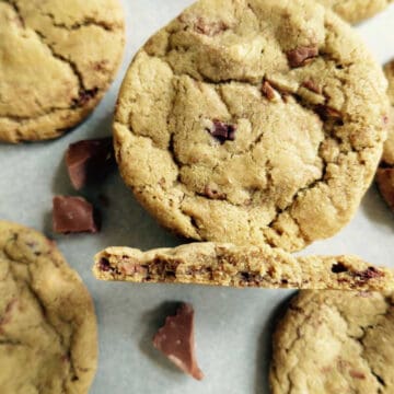 Chocolate chunk cookies on a baking tray. One of them has been broken in half and is on it's side.