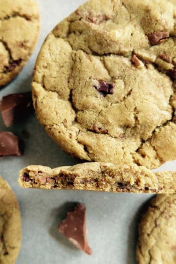 Chocolate chunk cookies on a baking tray. One of them has been broken in half and is on it's side.