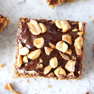 Top view of a peanut butter bar. It has glossy chocolate icing on it and is topped with chopped peanuts.