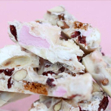 White chocolate rocky road pieces stacked on top of each other with a pink background which matches the pink marshmallows in the rocky road.